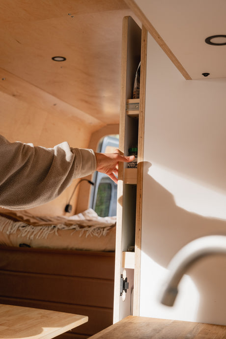 Space-saving design in an RV rental: a hand accesses a slim pull-out pantry with seasoning, highlighting clever camper storage.