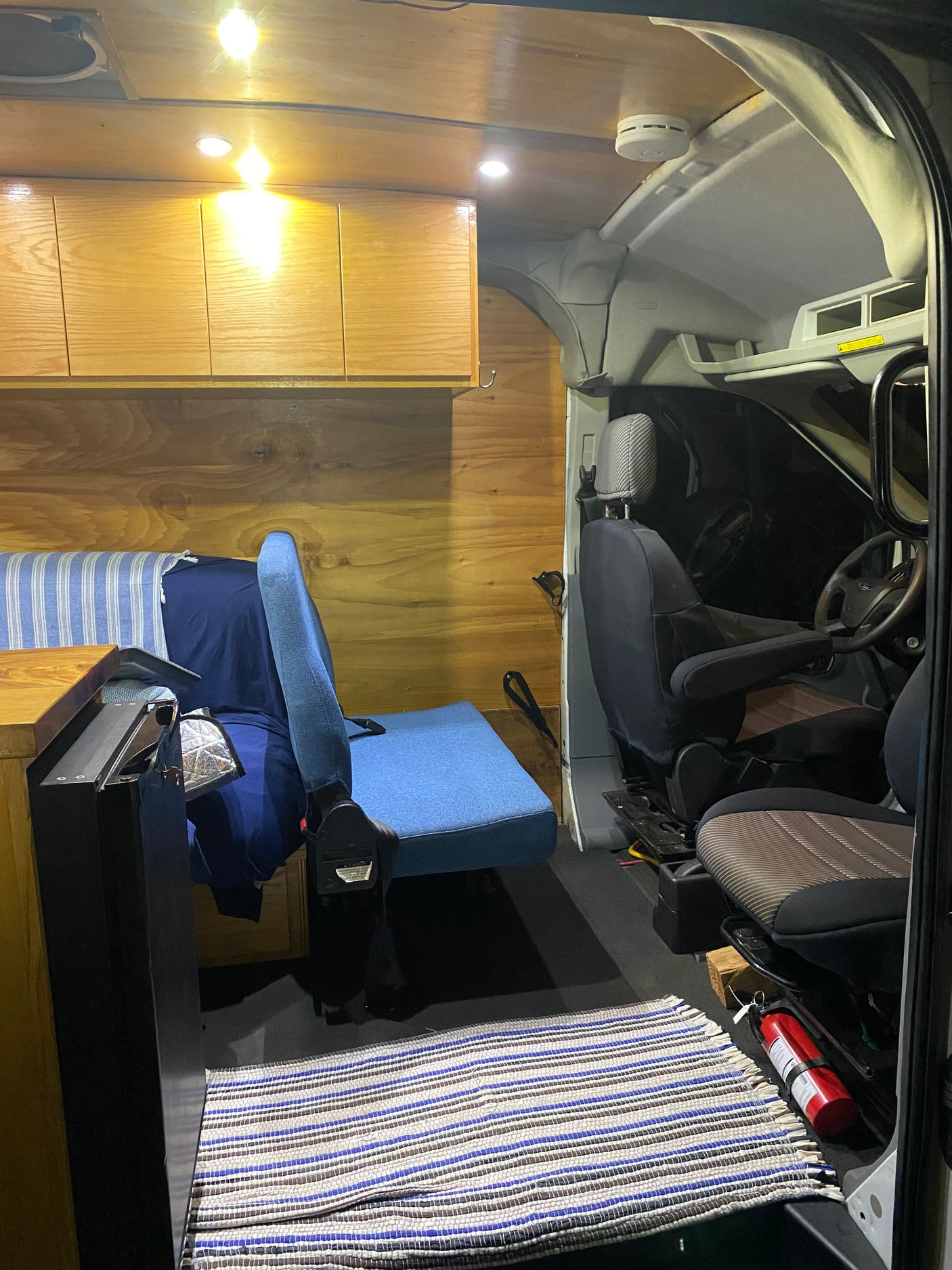 RV rental: Inside a converted camper van with warm wooden walls & cabinets, a cozy seating area, and front cabin views with a fire extinguisher.