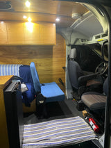 RV rental: Inside a converted camper van with warm wooden walls & cabinets, a cozy seating area, and front cabin views with a fire extinguisher.