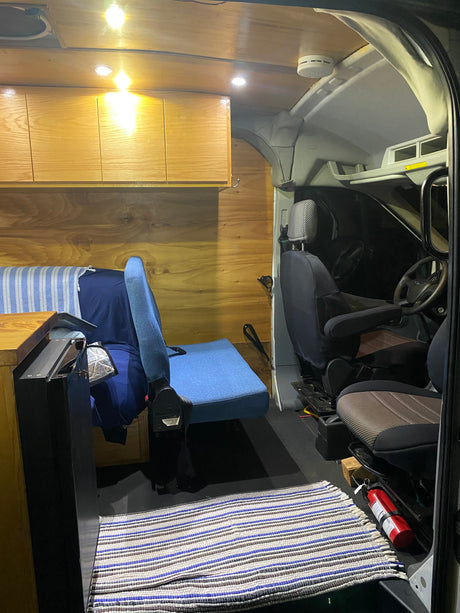 RV rental: Inside a converted camper van with warm wooden walls & cabinets, a cozy seating area, and front cabin views with a fire extinguisher.