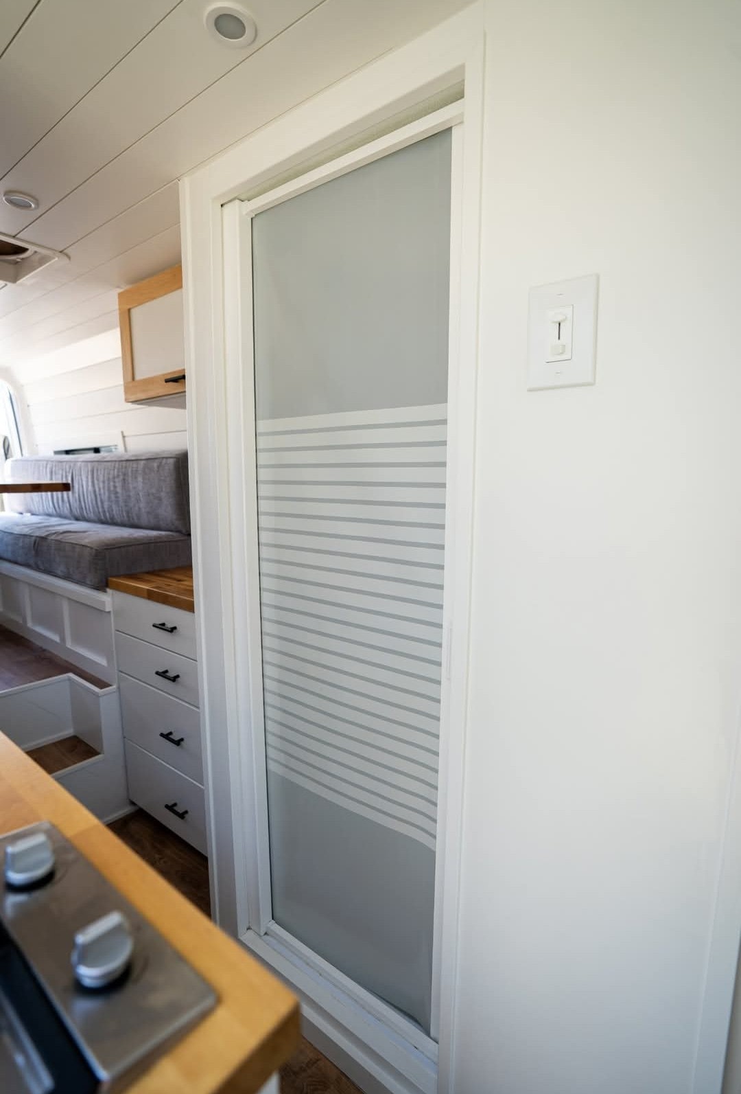 Functional RV rental interior with a compact kitchen area, seating, and a frosted glass door in a modern van conversion. — photo 9