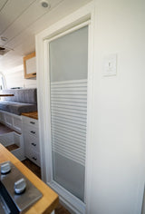 Functional RV rental interior with a compact kitchen area, seating, and a frosted glass door in a modern van conversion.