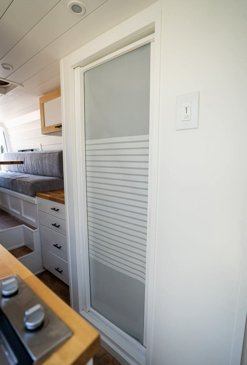 Functional RV rental interior with a compact kitchen area, seating, and a frosted glass door in a modern van conversion. — photo 9