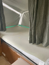 Pop-up RV rental bunk interior, with a mattress, gray curtains, and white fabric walls visible.