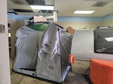 Little Guy teardrop RV rental with grey tent awning attached, set up indoors. Features an orange handle and front storage, ready for camping.