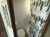 Compact RV rental bathroom featuring a toilet, decorative "RELAX" sign, and rustic wood-patterned shower curtain.