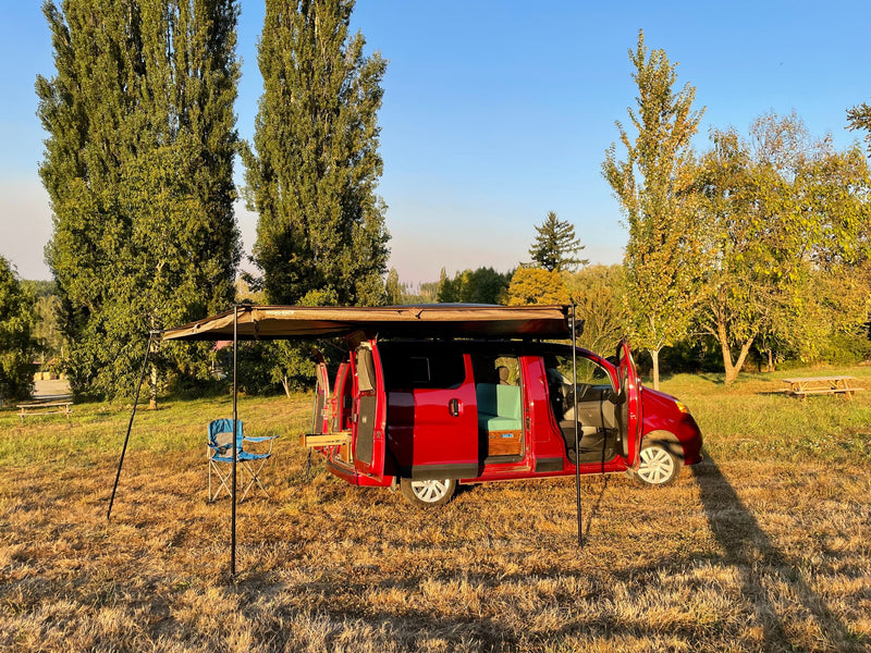 Red camper van RV rental set up with an awning and chair in a sunny field, ready for outdoor adventure. — photo 2
