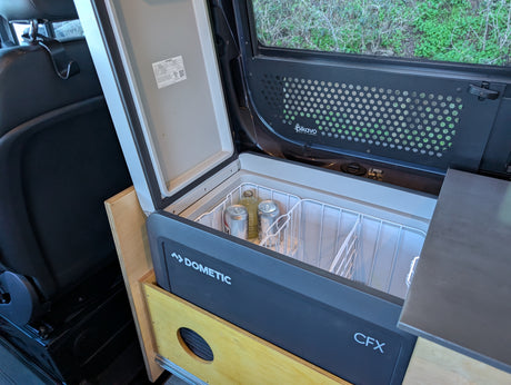 Open Dometic CFX portable fridge in a custom rv rental camper van, stocked with cold drinks for your adventure.