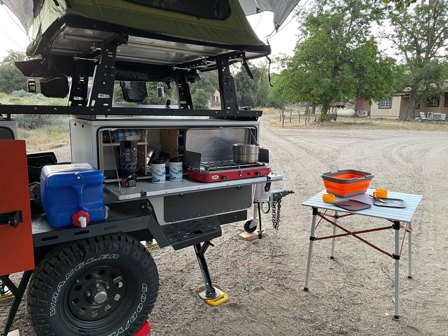 Off-road RV rental camping setup: trailer with rooftop tent, outdoor kitchen, and essential gear ready.