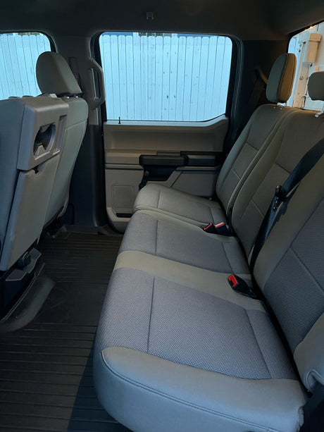 Inside an RV rental: rear passenger cabin with neat gray fabric seats, red seatbelt buckles, and dark rubber floor mats.