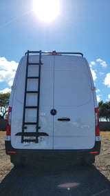 White Mercedes Sprinter van rv rental, seen from the rear, featuring a ladder and roof rack on a sunny day.