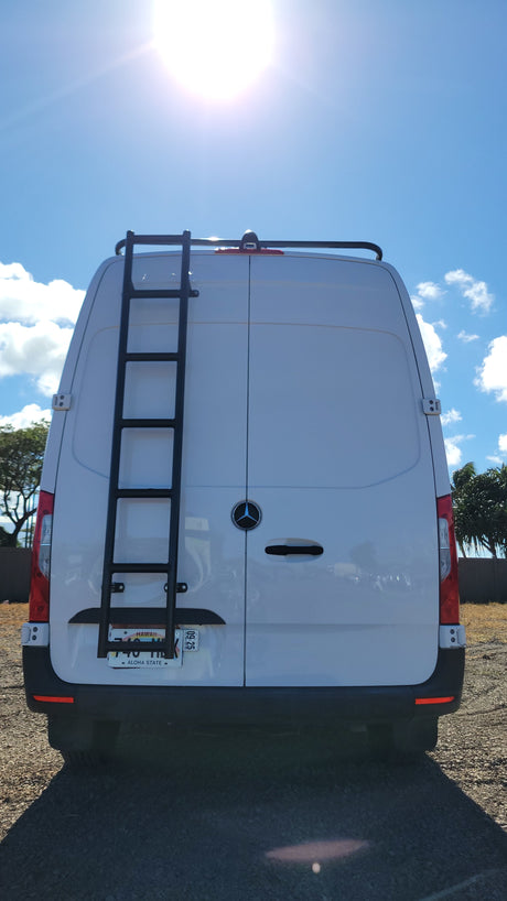 White Mercedes Sprinter van rv rental, seen from the rear, featuring a ladder and roof rack on a sunny day.