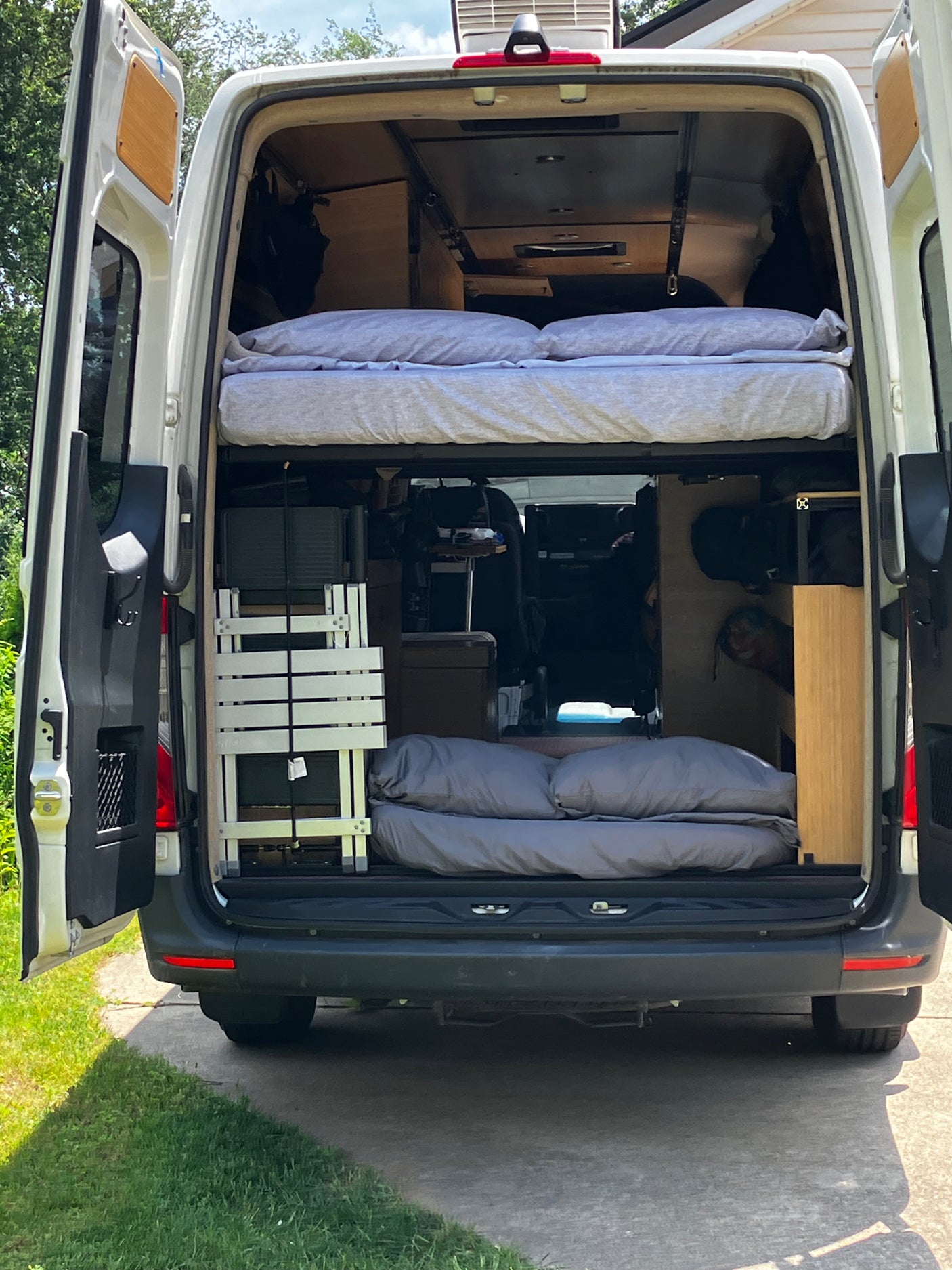 Rear view of an RV rental conversion van's interior, showing upper/lower beds, storage, and fold-out table. Ready for travel.