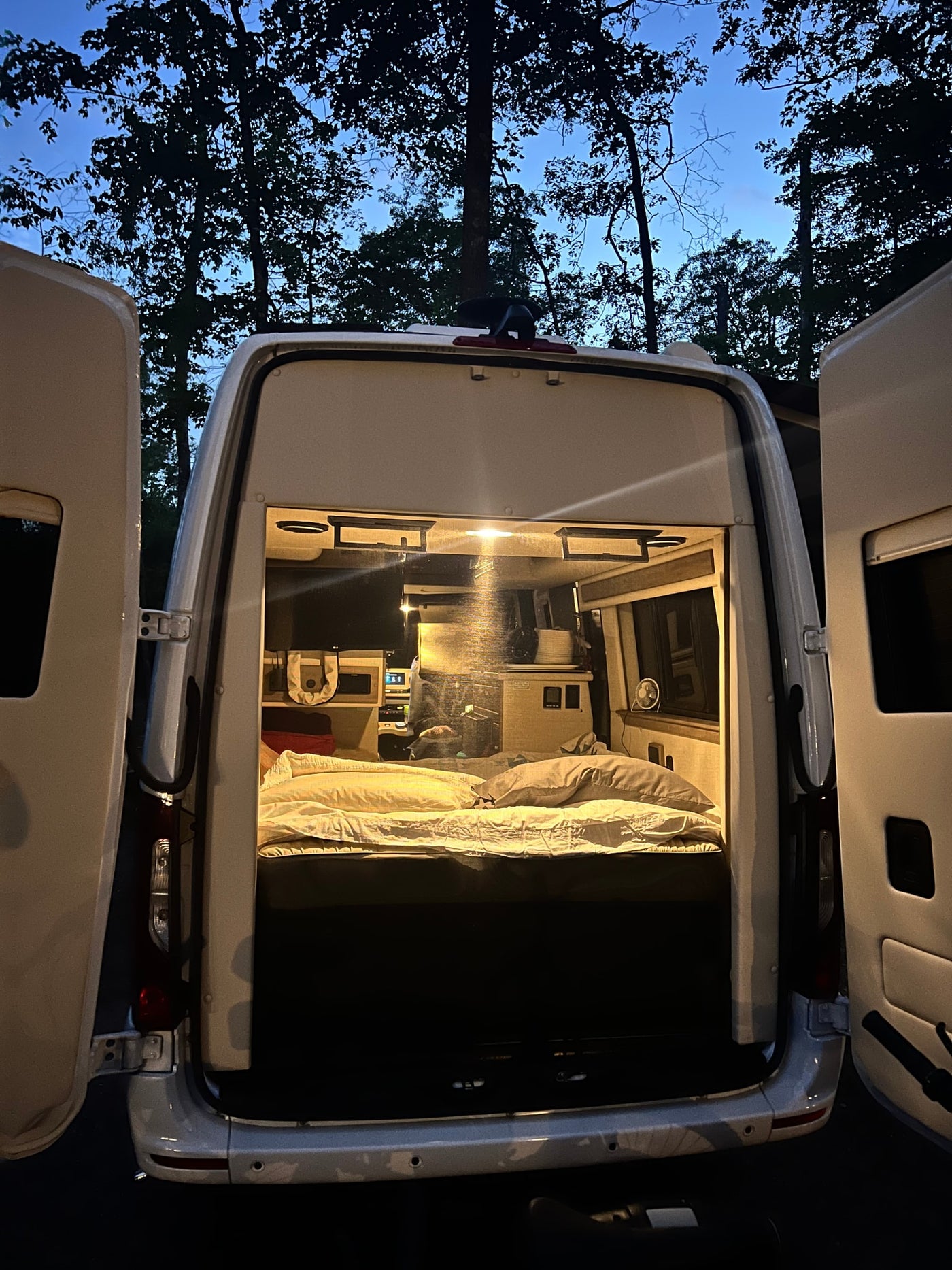 Cozy RV rental campervan with open rear doors at night, revealing a comfortable bed inside, perfect for camping. — photo 9