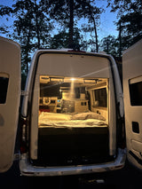 Cozy RV rental campervan with open rear doors at night, revealing a comfortable bed inside, perfect for camping.