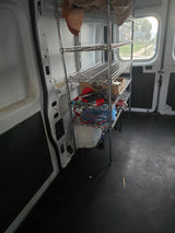 Interior of a white utility van, possibly for rv rental. Chrome shelving unit holds supplies; black textured floor.