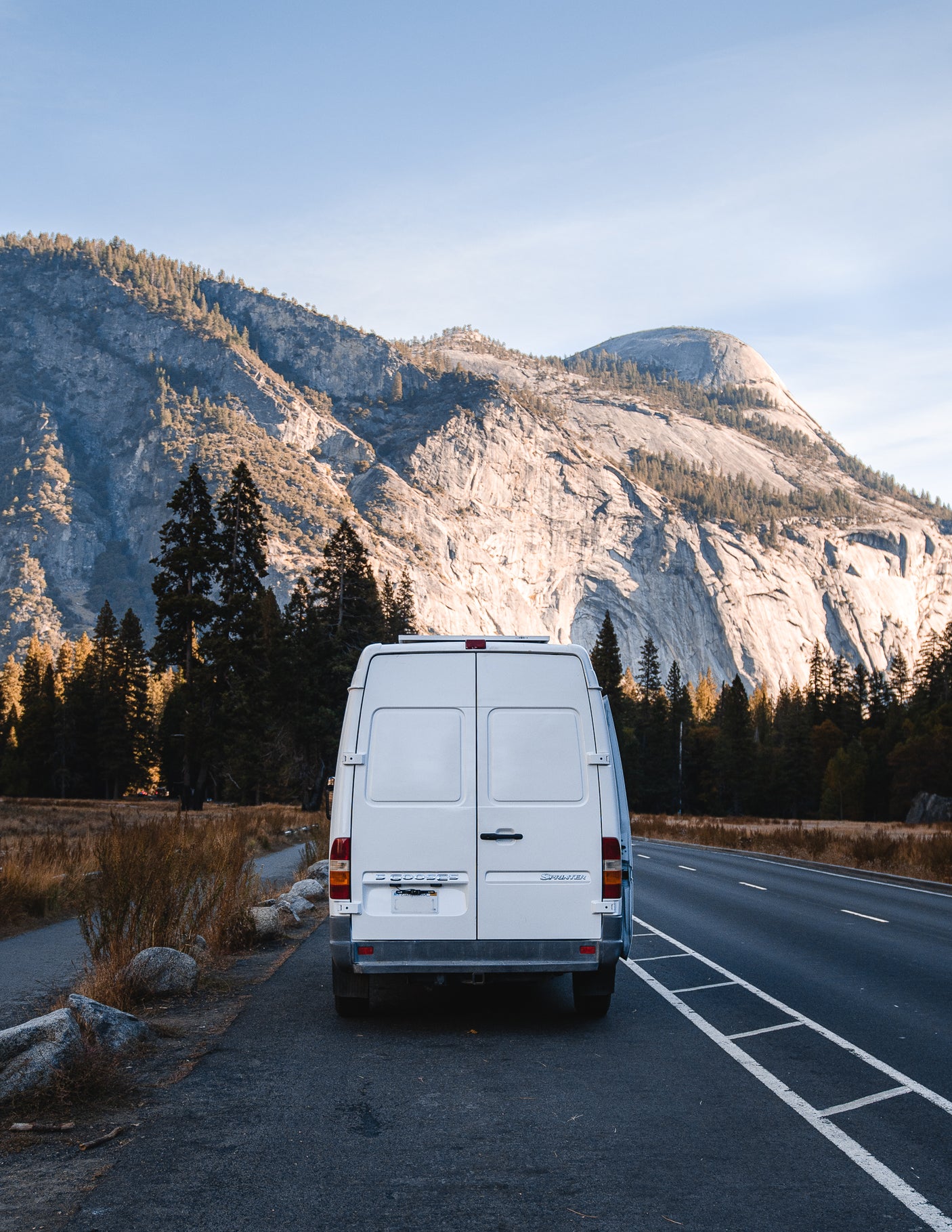White Sprinter van (RV rental) on a scenic road with vast mountains & forests. Perfect for road trips & adventure.