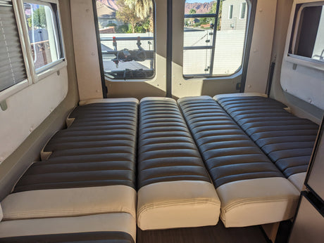 Spacious RV rental interior with comfortable modular bedding. Windows show desert mountains & outdoor rack.
