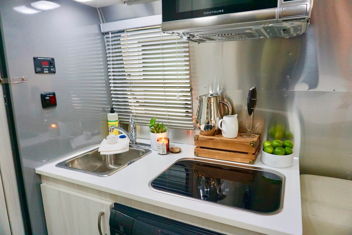 Inside a modern **rv rental** kitchen, featuring a stainless steel sink, covered cooktop, microwave, and stylish counter accessories. — photo 14