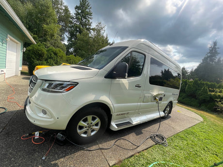 White Mercedes-Benz Sprinter camper van (RV rental) parked on a driveway, hooked up to power.