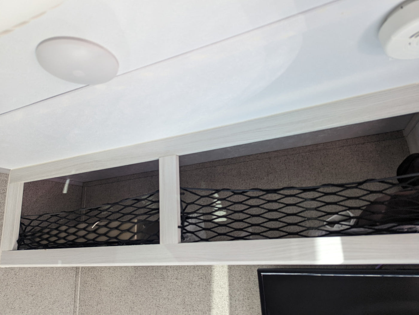 RV rental interior: overhead storage compartments with elastic netting for securing items, a ceiling light, and a smoke detector. — photo 10