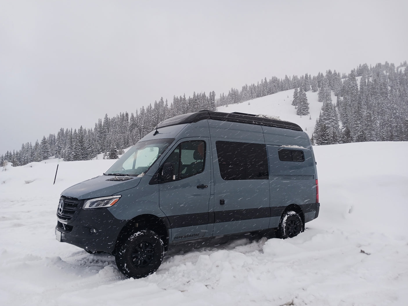 Grey Mercedes Sprinter adventure van, perfect for an RV rental, parked in deep snow with snowy trees.