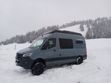 Grey Mercedes Sprinter adventure van, perfect for an RV rental, parked in deep snow with snowy trees.