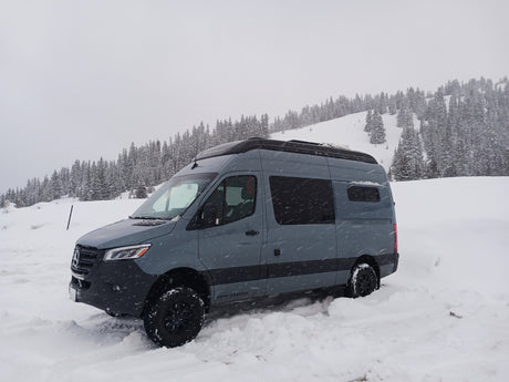 Grey Mercedes Sprinter adventure van, perfect for an RV rental, parked in deep snow with snowy trees.