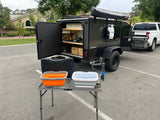 RV rental: Compact overland camper trailer with outdoor kitchen, wash basins, and attached pickup truck, parked in a lot.