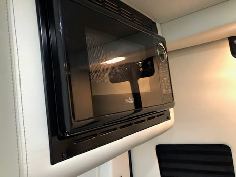 Brightly lit black microwave oven, seamlessly integrated into an RV rental's interior for your convenience.