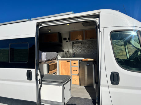 Inside this RV rental camper van: custom interior with kitchen, bed, fridge, and storage, ready for adventure.