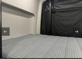 Inside an RV rental: a grey patterned mattress in a compact sleeping area with black fabric walls, ready for your adventure.