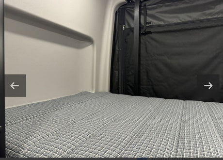 Inside an RV rental: a grey patterned mattress in a compact sleeping area with black fabric walls, ready for your adventure.