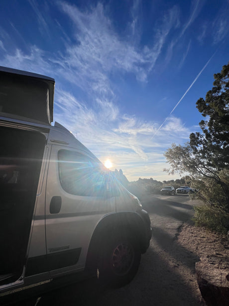 Experience van life! This RV rental camper van, door open, is parked for golden hour views in a rugged, natural landscape.