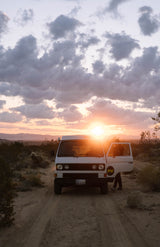 RV rental white VW camper van on a desert road at sunset. A person steps out, sun bright. Ideal for a road trip adventure!