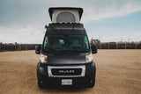 A black Ram ProMaster camper van with a raised pop-top roof, parked on a dirt lot. Explore with this RV rental!