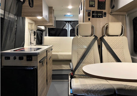 Detailed view of an RV rental interior: compact kitchen, swiveling front seats with table, and rear bench seating.