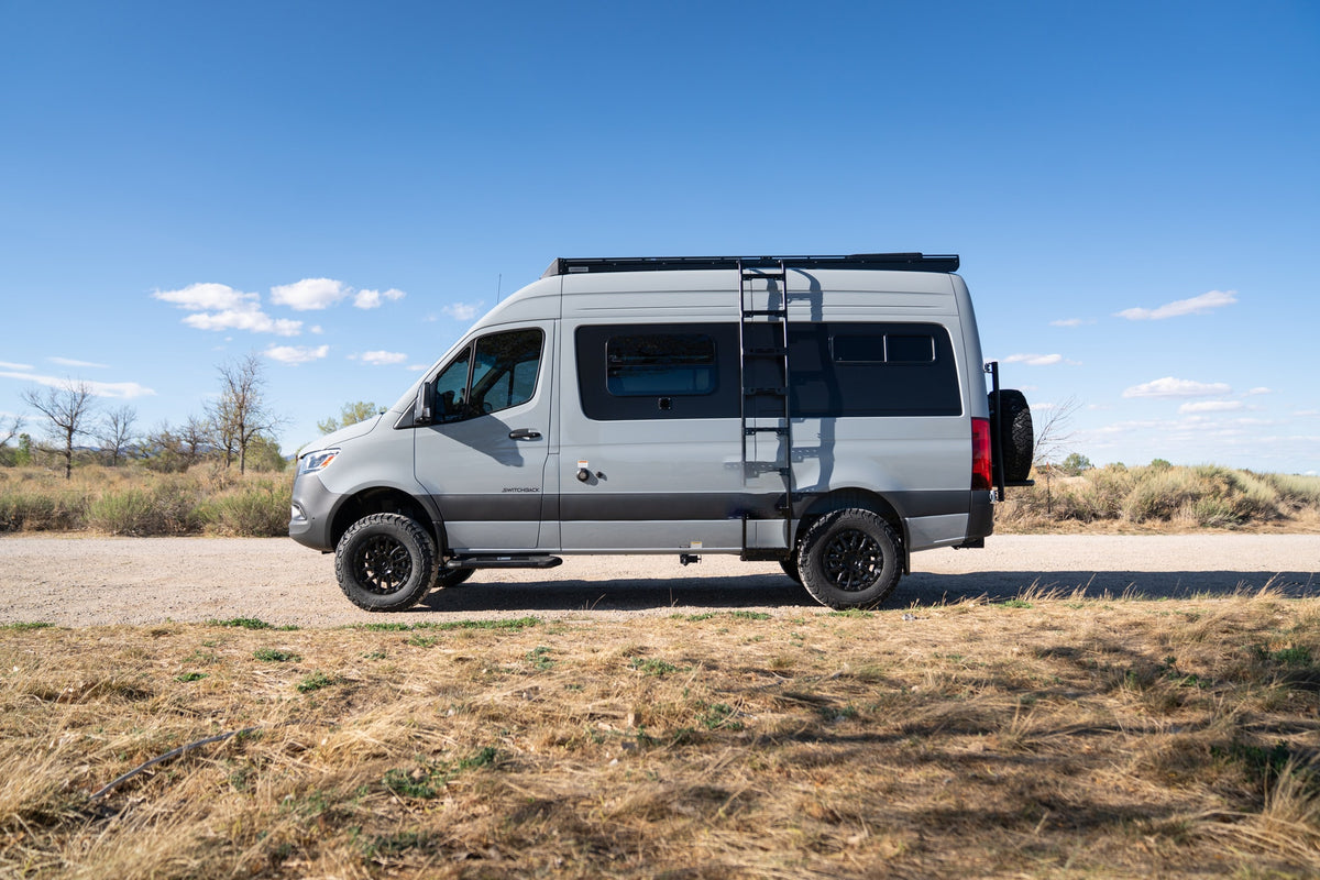 Gray adventure camper van with off-road tires, ladder, and roof rack parked on a dirt road, perfect for RV rental. — photo 3