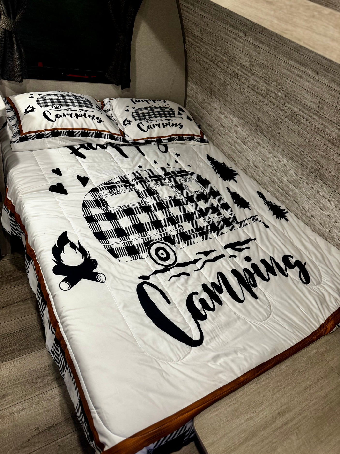 Camping-themed bedding with a plaid RV, trees, and campfire in a cozy RV rental.