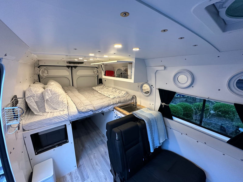  and passenger seating area. Wood-look floors and ample lighting create a comfortable living space.|RV rental: Spacious camper van interior with large rear bed — photo 9