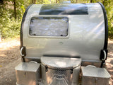 This RV rental shows the rear of a silver teardrop trailer with a top solar panel and three diamond plate storage boxes below.