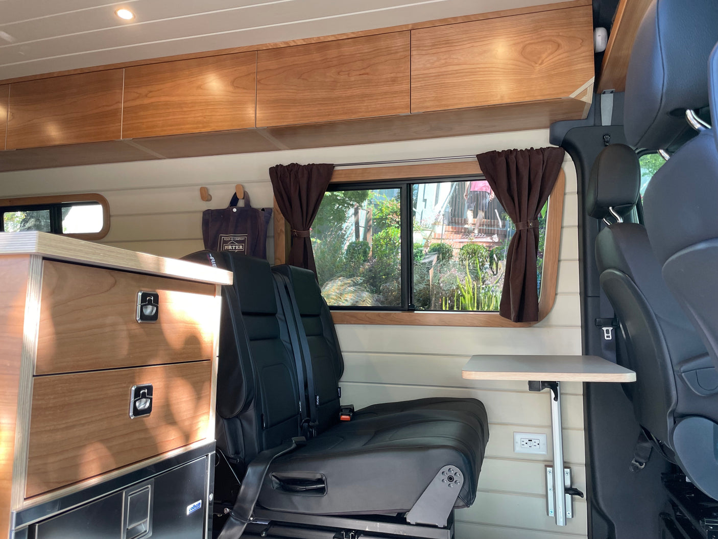 This **rv rental** interior features light wood cabinetry, seating, a fold-out table, and a large window with brown curtains.