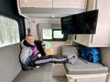 A happy boy smiles while relaxing inside a modern RV rental, enjoying the comfortable seating and TV, with snowy trees visible outside.