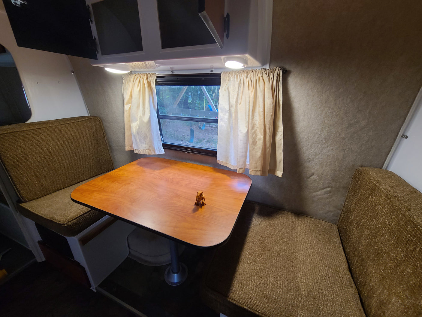 RV rental dinette featuring a wooden table, cushioned benches, window with curtains, and overhead cabinets.