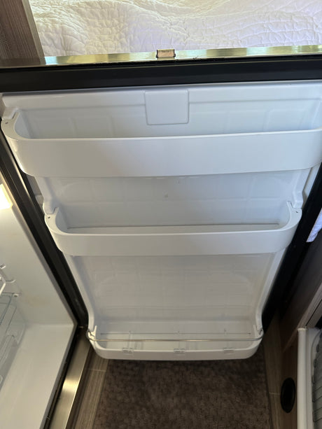 Open RV rental refrigerator door showing compact interior shelves and storage. Ready for your trip!