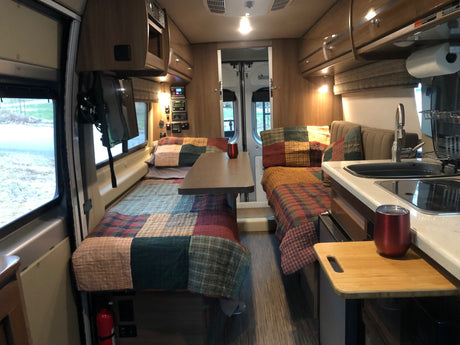 This RV rental's inviting interior features twin beds, a central table, and a functional kitchen area.