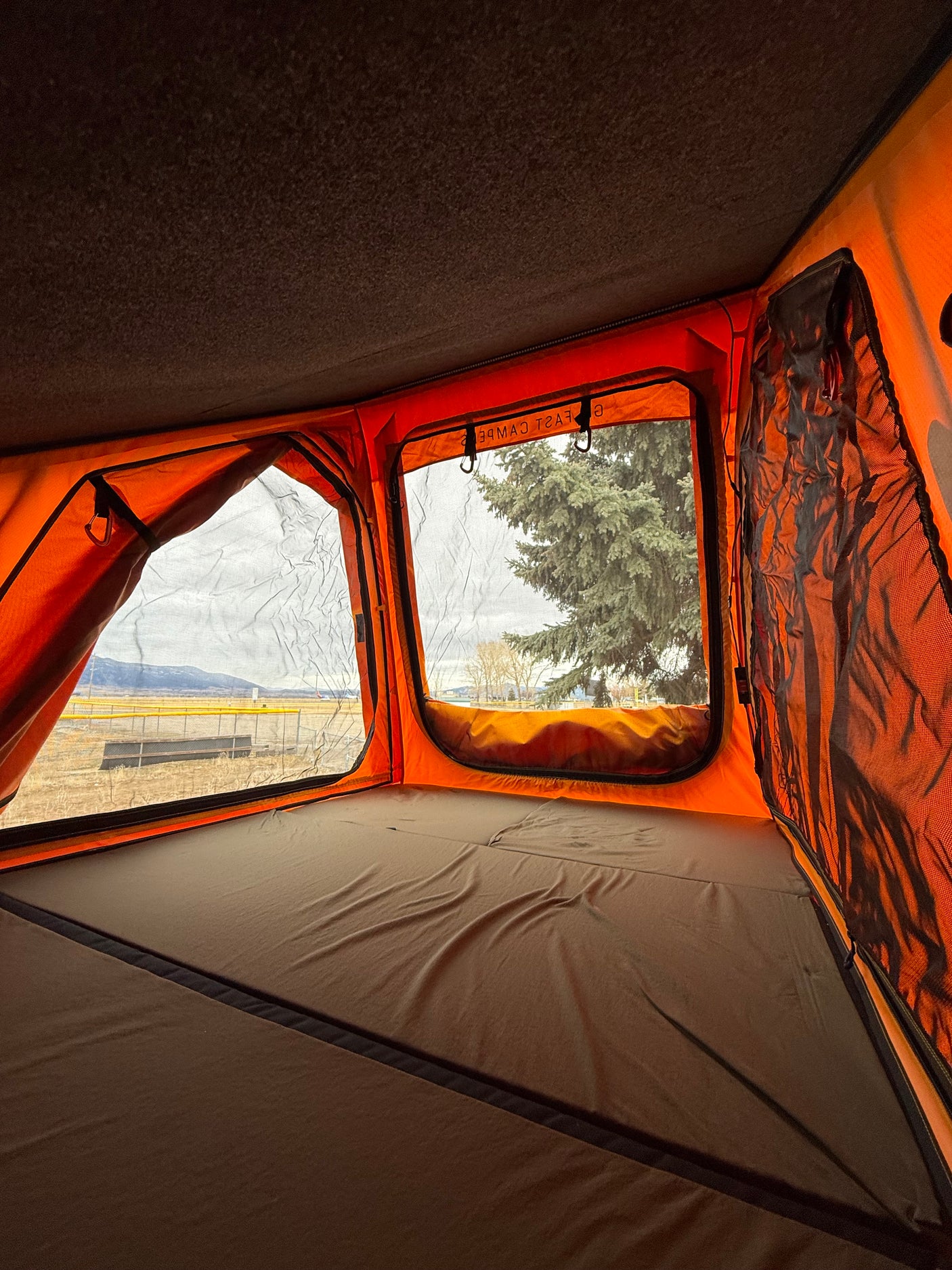 Inside a cozy orange rooftop tent with a comfortable bed, offering scenic mountain views. Ideal for your RV rental adventure.