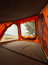 Inside a cozy orange rooftop tent with a comfortable bed, offering scenic mountain views. Ideal for your RV rental adventure.