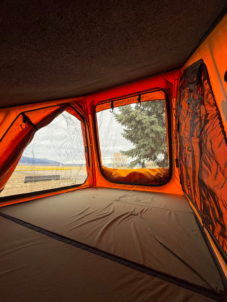 Inside a cozy orange rooftop tent with a comfortable bed, offering scenic mountain views. Ideal for your RV rental adventure.