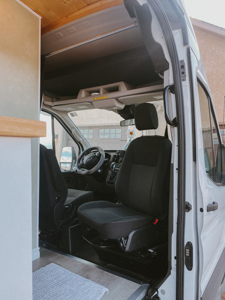 RV rental interior: The bright driver's cabin with black seats & Ford steering wheel, seen from the converted living space.